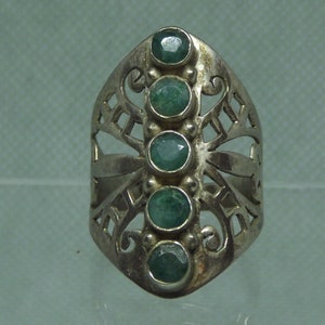 May include: A silver ring with a filigree design and five green gemstones.