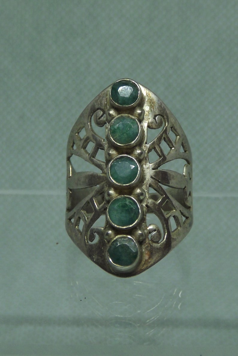 May include: A silver ring with a filigree design and five green gemstones.