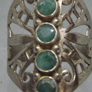 May include: A silver ring with a delicate, openwork design featuring five green gemstones. The ring has a unique, butterfly-like shape.