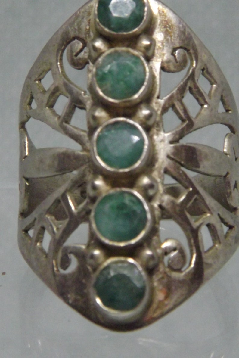 May include: A silver ring with a delicate, openwork design featuring five green gemstones. The ring has a unique, butterfly-like shape.