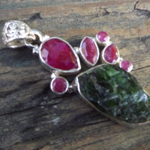 May include: A silver pendant with a large green gemstone and several smaller pink gemstones. The pendant has a detailed silver bail.