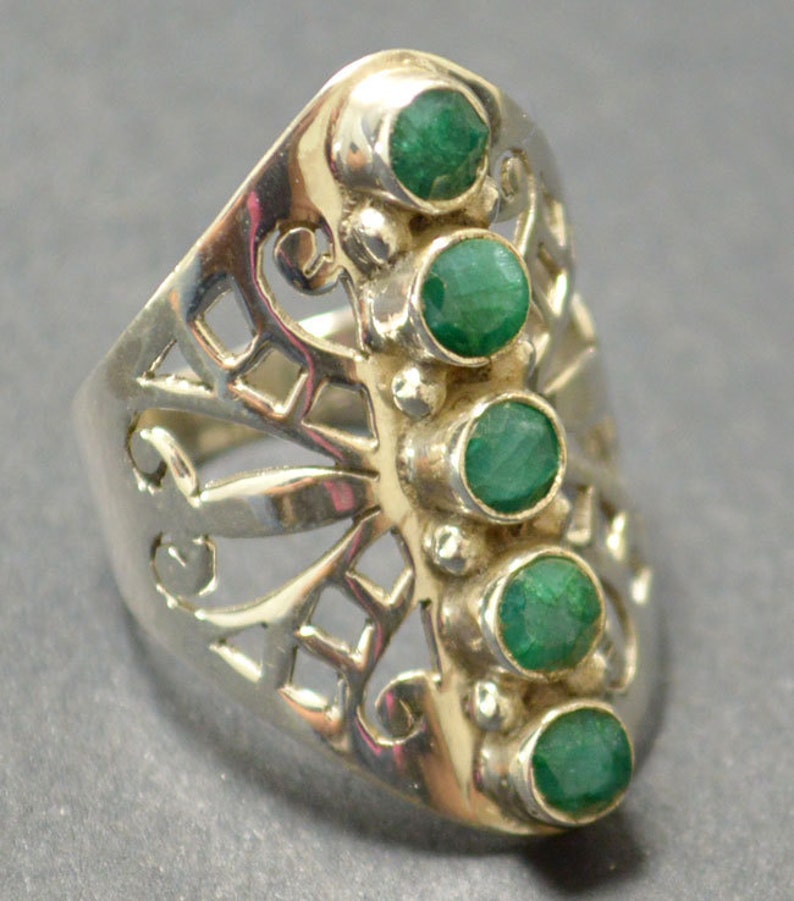 May include: A silver ring with a delicate, openwork design and five emerald green gemstones set in a row.