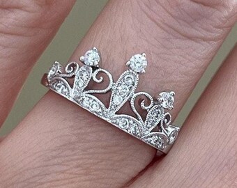 May include: A silver crown ring with clear cubic zirconia stones. The ring is delicate and intricate, with a floral design.