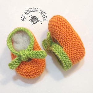 May include: A pair of orange knit baby booties with bright green trim and a decorative bow detail on the front. The text PDF DOWNLOAD PATTERN is visible above the booties, accompanied by a small graphic of a ball of yarn with knitting needles.