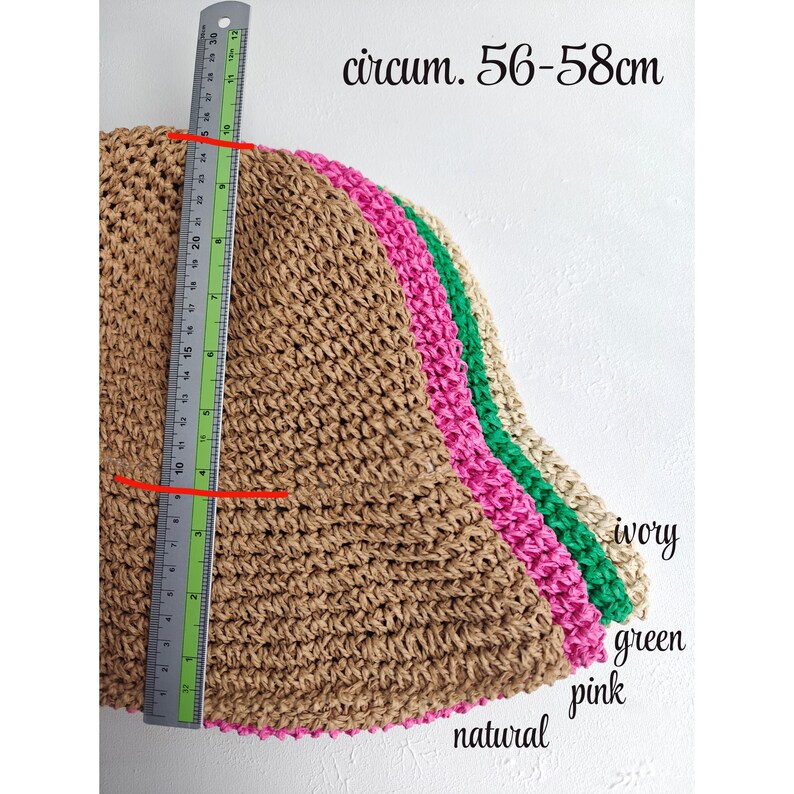 May include: A stack of woven straw hats in natural, pink, green, and ivory. The hats have a circumference of 56-58cm. A ruler is placed next to the hats to measure the height. The hats are suitable for sun protection.
