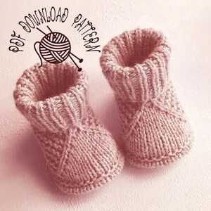 May include: A pair of dusty pink knitted baby booties featuring a ribbed cuff and a textured stitch pattern on the foot. The text PDF DOWNLOAD PATTERN is printed above the booties, accompanied by a graphic illustration of a ball of yarn.