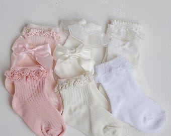 May include: A set of six baby socks with lace trim and satin bows. The socks are in pink, white, and ivory.