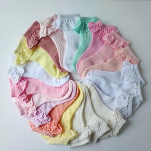 Könnte beinhalten: Eine Sammlung von 15 Paar weißen Baumwollsocken mit Spitzenbesatz in verschiedenen Pastellfarben, darunter Rosa, Gelb und Grün. Die Socken sind in einem Kreis angeordnet.