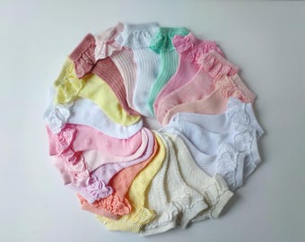May include: A collection of 15 pairs of white cotton socks with lace trim in various pastel colours, including pink, yellow, and green. The socks are arranged in a circle.
