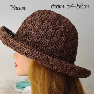 May include: A brown crocheted hat with a brim, shown in profile. The hat has a textured pattern and the text "Brown" and "circum. 54-56cm" are visible. The hat is approximately 21.25-22 inches in circumference.
