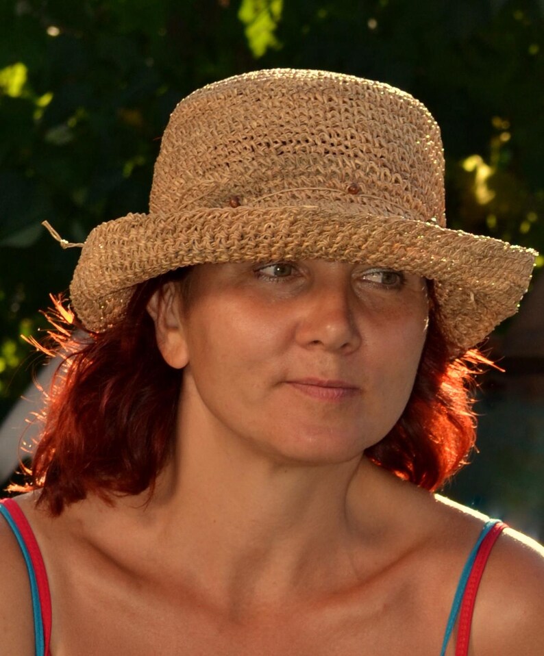 May include: A woven straw hat with a wide brim. The hat is a light tan color and has a slightly rounded crown. The person is wearing a red and blue top.