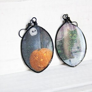 May include: A pair of Halloween-themed earrings with black wire frames. One earring features a glittery image of a jack-o'-lantern, while the other features a glittery image of a black cat.