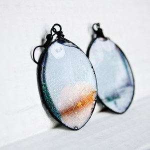 May include: A pair of silver and gold glitter resin earrings with black wire hooks. The earrings are oval shaped and have a white background with a gold and silver glitter design.