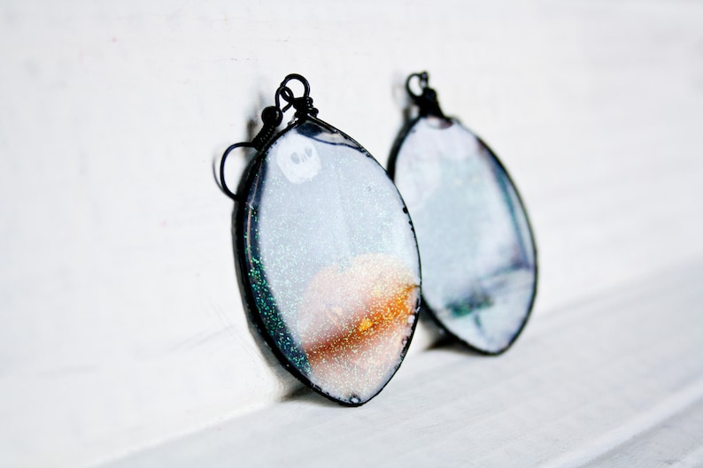 May include: A pair of silver and gold glitter resin earrings with black wire hooks. The earrings are oval shaped and have a white background with a gold and silver glitter design.