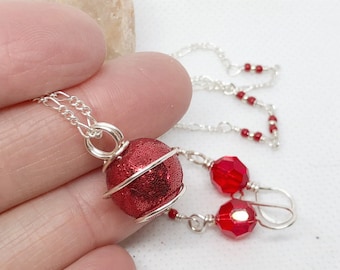 May include: A red glitter ball necklace with a silver chain and matching red crystal earrings. The necklace features a silver wire wrapped around the ball.