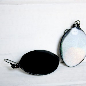 May include: A pair of earrings, one with a black oval-shaped glass cabochon and the other with a white oval-shaped glass cabochon with iridescent glitter.