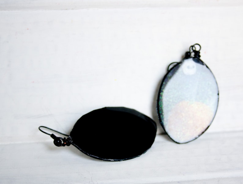 May include: A pair of earrings, one with a black oval-shaped glass cabochon and the other with a white oval-shaped glass cabochon with iridescent glitter.
