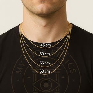 K&ouml;nnte beinhalten: Ein Mann tr&auml;gt ein schwarzes T-Shirt mit goldenen Halsketten in verschiedenen L&auml;ngen: 45 cm, 50 cm, 55 cm und 60 cm. Die Halsketten werden vor einem hellen Hintergrund pr&auml;sentiert. Das T-Shirt tr&auml;gt den Text "MYTHICS ATELIER".