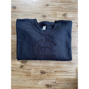 May include: Black sweatshirt with a black embroidered logo that says "ONYX STORM" and "BRAVE THE DARK".