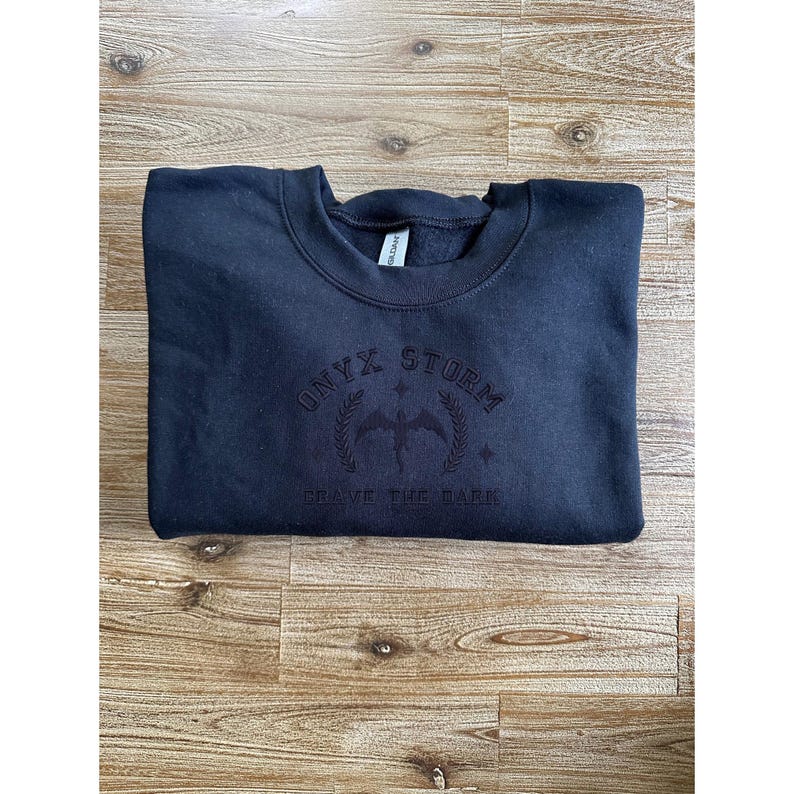 May include: Black sweatshirt with a black embroidered logo that says "ONYX STORM" and "BRAVE THE DARK".