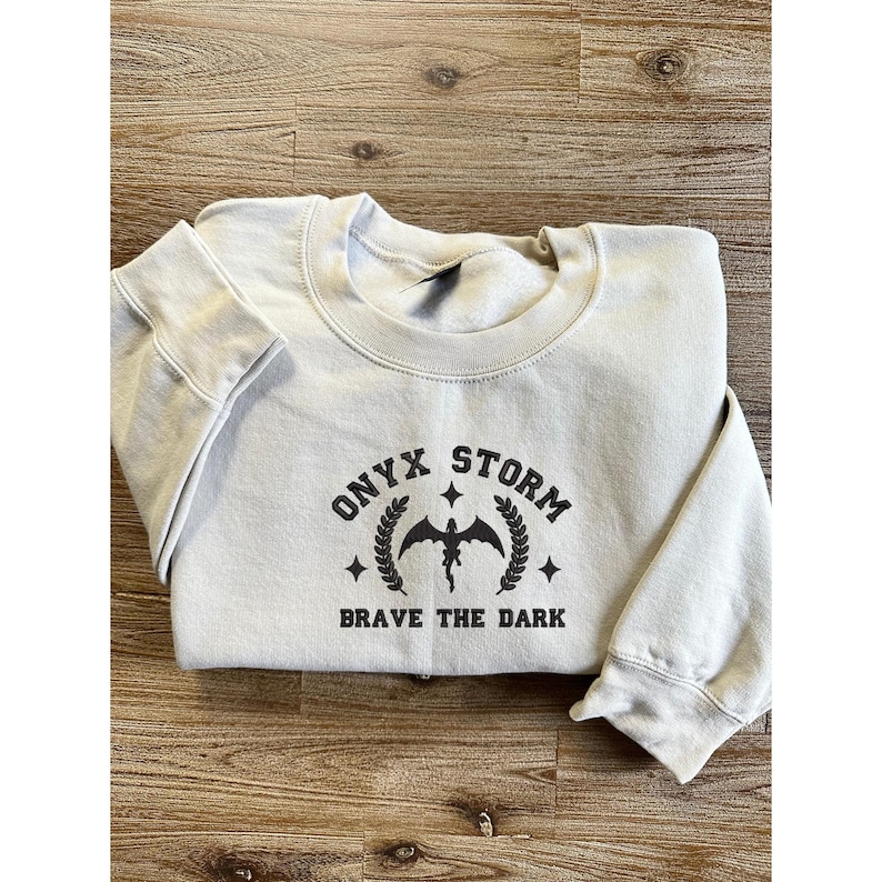 May include: A light gray sweatshirt with a black graphic print of a dragon with the text "ONYX STORM" and "BRAVE THE DARK" on it.