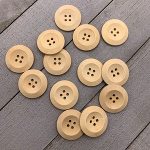 May include: A collection of 12 wooden buttons in various sizes and shapes. The buttons are all a light brown color and have four holes each.