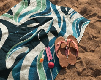 May include: A beach towel with a blue and green wave pattern and a black orca whale design.  There are two pairs of pink flip flops with white polka dots, two nail files, and a bottle of nail polish on the towel.