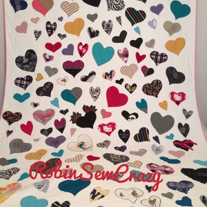 May include: A white quilt with a pink border, featuring a large number of colorful heart-shaped patches. The hearts are made from different fabrics and have various designs, including stripes, polka dots, and animal prints. The quilt is signed "Robin Sew Crazy" in the lower center.
