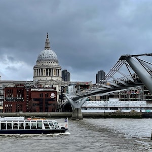 Può includere: Una barca turistica bianca sul Tamigi a Londra, in Inghilterra. La barca sta viaggiando verso la telecamera con la Cattedrale di San Paolo sullo sfondo. Il Millennium Bridge è in primo piano.