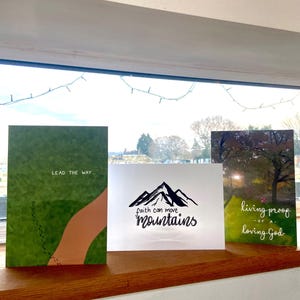 Könnte beinhalten: Drei Karten mit inspirierenden Zitaten. Die erste Karte ist grün mit einem braunen Weg und dem Text "Lead the way". Die zweite Karte ist weiß mit schwarzem Text, der "Faith can move mountains" lautet. Die dritte Karte ist weiß mit schwarzem Text, der "Living proof of a loving God" lautet.