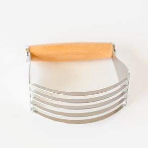 May include: A silver pastry cutter with a wooden handle. The cutter has five blades and is used for cutting butter into flour.