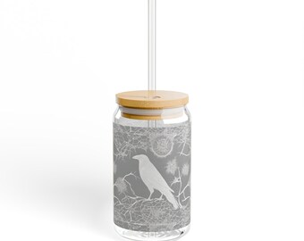 May include: A glass drinking jar with a gray and white design of a bird and branches. The jar has a bamboo lid and a clear glass straw.