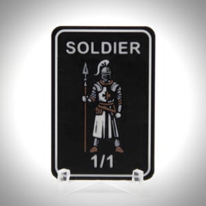 May include: Black rectangular card with rounded corners featuring a medieval soldier illustration. The word "SOLDIER" is at the top, and "1/1" is at the bottom. The soldier is in silver armour, holding a spear.