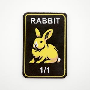 May include: A rectangular patch with rounded corners featuring a yellow rabbit illustration on a black background. The word "RABBIT" is printed in white at the top, with "1/1" at the bottom.