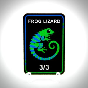 May include: A rectangular black card with rounded corners featuring a green and blue striped lizard illustration in the centre. The text FROG LIZARD is printed in white at the top, and the number 3/3 is printed in white at the bottom of the card.