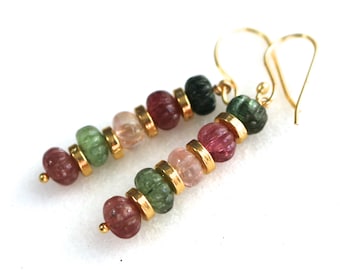 May include: A pair of dangle earrings featuring a combination of colorful, carved gemstone beads in shades of pink, green, and burgundy. The beads are separated by gold-colored metal rings and suspended from gold-colored ear wires.