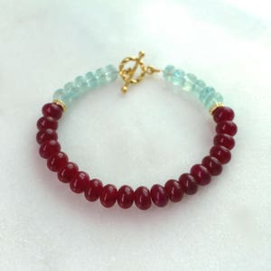 May include: A gold clasp bracelet with red and blue gemstone beads. The bracelet is made with a toggle clasp.