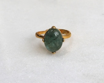May include: A gold ring with a large oval-shaped green gemstone. The ring has a simple band and the gemstone is set in a bezel setting.