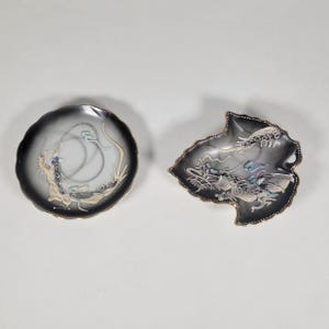 May include: Two small ceramic plates with a black and white background and gold trim. Both plates feature a dragon design with colorful accents.