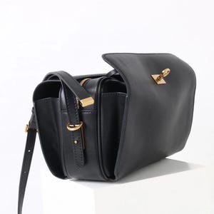 May include: Black leather crossbody bag with a flap closure and gold-toned hardware. The bag features a long, adjustable strap and a zippered compartment. The design includes a rectangular shape with a structured silhouette, suitable for everyday use.