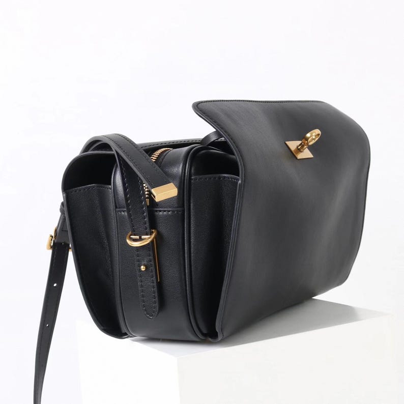 May include: Black leather crossbody bag with a flap closure and gold-toned hardware. The bag features a long, adjustable strap and a zippered compartment. The design includes a rectangular shape with a structured silhouette, suitable for everyday use.