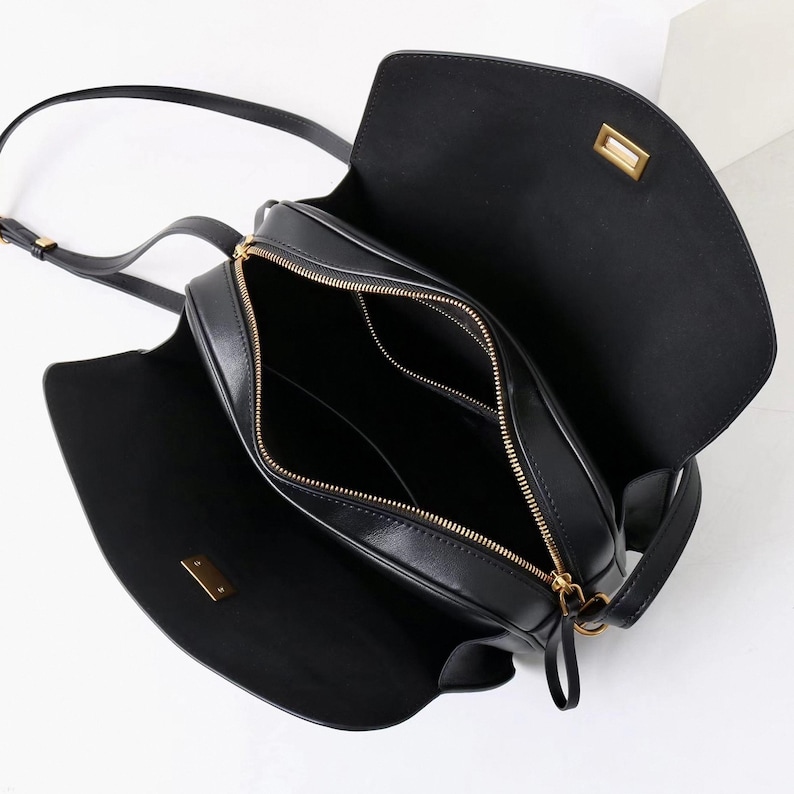 May include: Black leather crossbody bag with a flap closure and gold-toned hardware. The bag has a long adjustable strap and a zippered main compartment. The interior is black and features a small pocket.