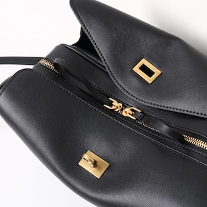 May include: Black leather handbag with gold-toned hardware. The bag features a flap closure with a rectangular clasp and a zippered compartment. The zipper and other hardware are gold-colored.