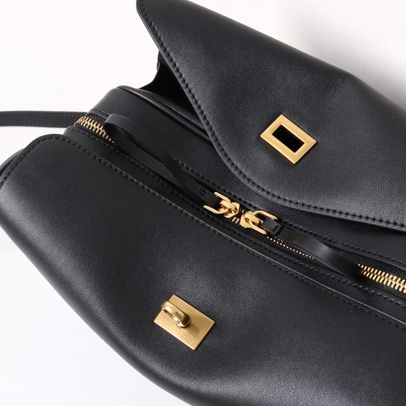 May include: Black leather handbag with gold-toned hardware. The bag features a flap closure with a rectangular clasp and a zippered compartment. The zipper and other hardware are gold-colored.