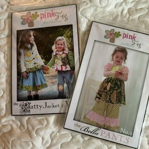 May include: Two packaged sewing patterns from "pink fig patterns" featuring children's clothing. One pattern is for "the Patty Jacket & Vest", and the other is for "the Bella Pants". The patterns show children wearing the finished garments.