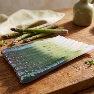 Op de afbeelding: Een rechthoekig glazen serveerplateau met een gegoten ontwerp dat een bundel verse asperges nabootst. Het plateau vertoont een kleurverloop van diep bosgroen bij de punten tot een lichtroze kleur aan de onderkant van de stengels.