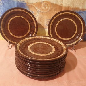 May include: A stack of ten brown ceramic plates with a white rim. The plates have a brown and white concentric circle design.