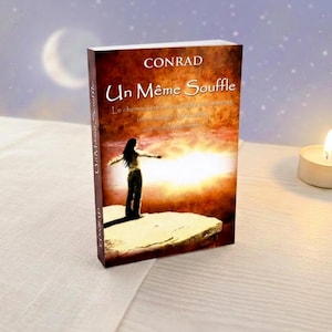 Peut inclure: Un livre intitulé "Un Même Souffle" de Conrad, avec une femme sur la couverture. La couverture présente un arrière-plan chaleureux, semblable à un coucher de soleil. Une bougie allumée est à droite du livre.