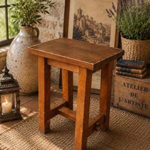 May include: A rectangular wooden stool with a medium brown finish, featuring four straight legs connected by a lower support brace. The stool has a flat, solid top surface and a sturdy construction with visible wood grain and minor surface wear.