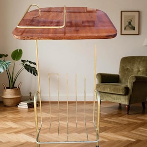 Peut inclure: Un porte-revues vintage doté d'un plateau en bois poli avec une poignée en laiton et une section inférieure composée de fines tiges en laiton. La structure est soutenue par un cadre en laiton avec quatre petits pieds, conçu pour maintenir les périodiques.